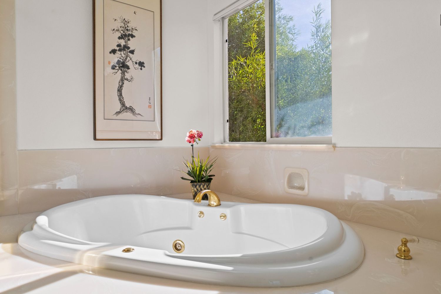 Luxurious oval soaking tub with gold fixtures, garden view window, and Asian wall art.