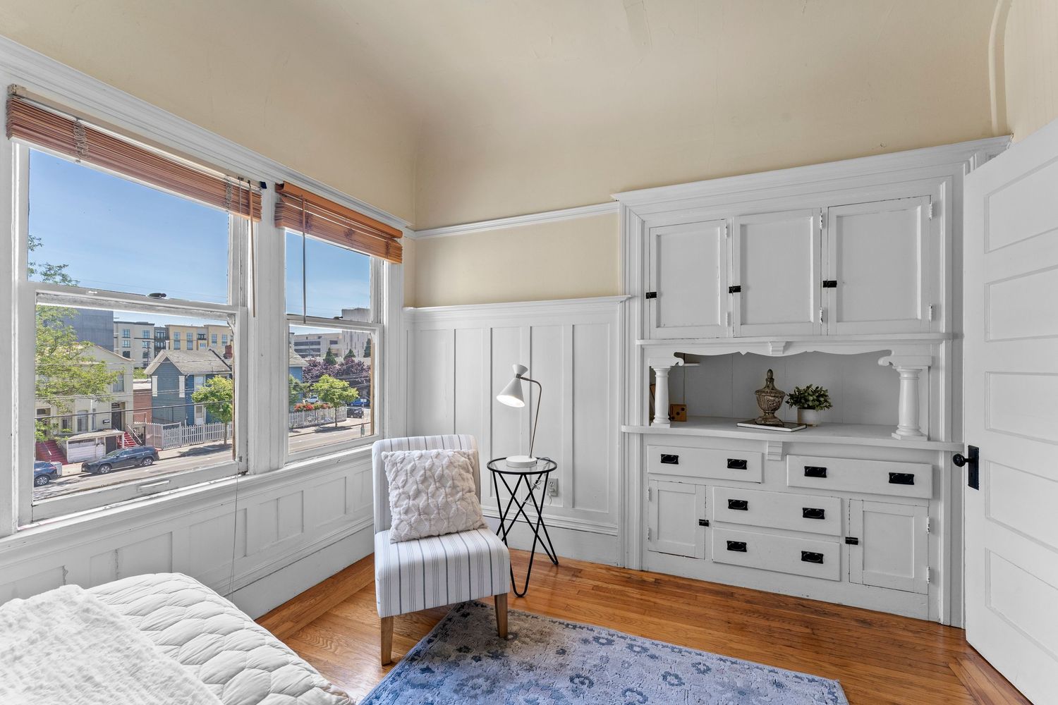 Charming bedroom with white built-in cabinetry, hardwood floors, and neighborhood views.