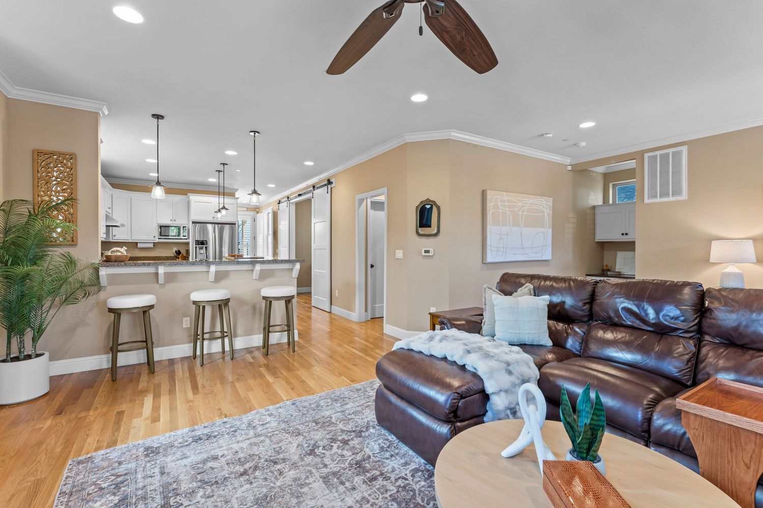 Open-concept living room with leather sofa, hardwood floors, kitchen bar seating, and recessed lighting.