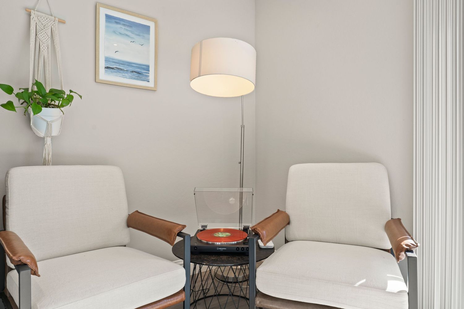 Minimalist sitting nook with two white accent chairs, floor lamp, and coastal wall art.