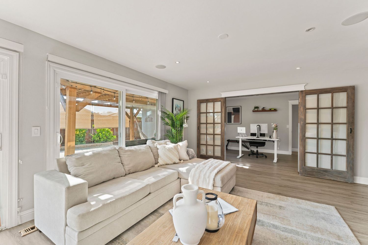 Airy living room with white sofa, sliding barn doors, home office nook, and patio access.