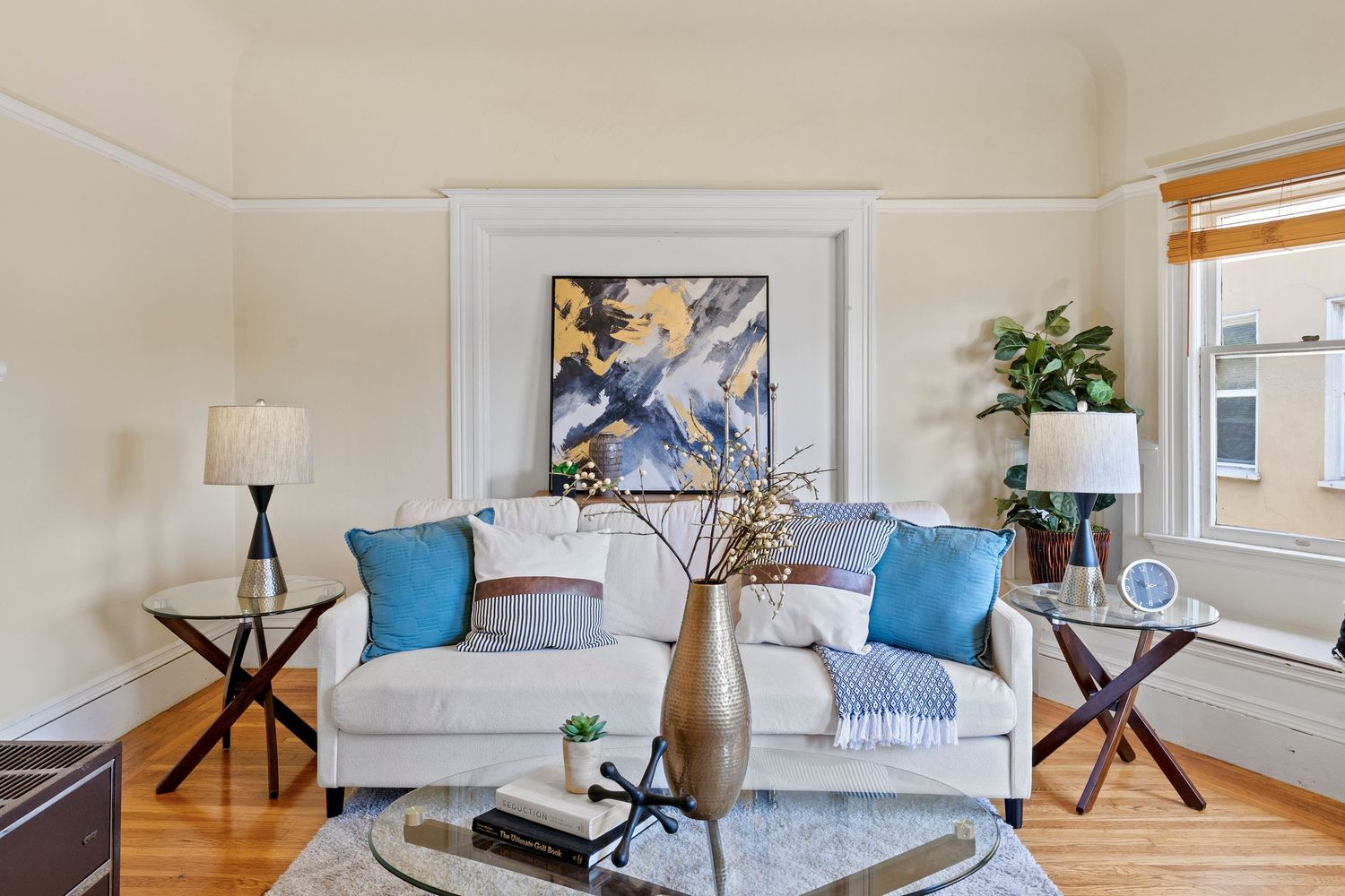 Bright living room with white sofa, blue accent pillows, abstract wall art, and hardwood floors.