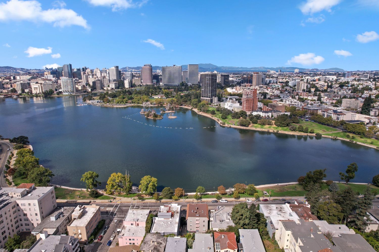 Aerial view of Lake Merritt in Oakland, CA surrounded by urban cityscape and blue skies.