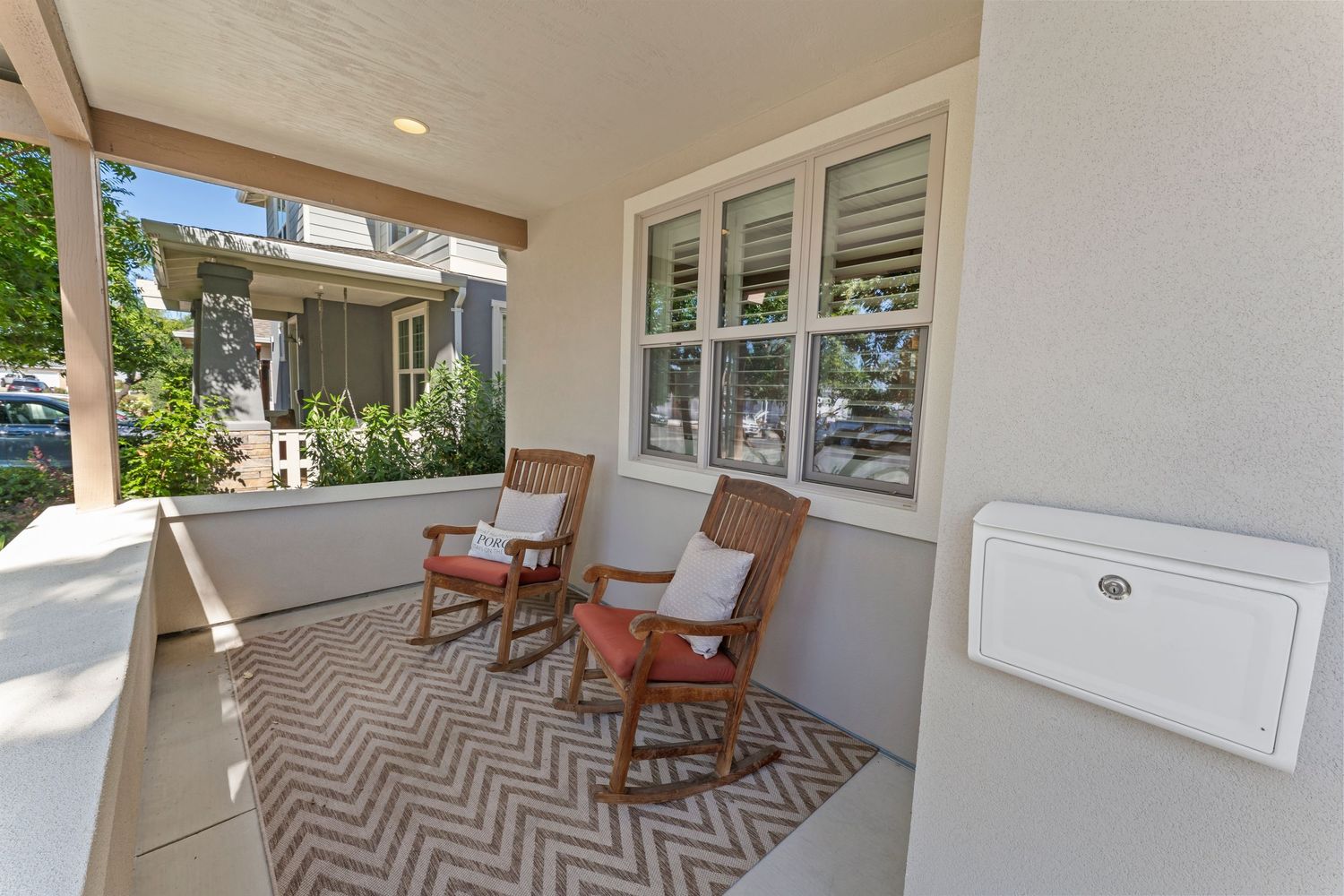 Charming covered front porch with two rocking chairs, chevron rug, and plantation shuttered windows.