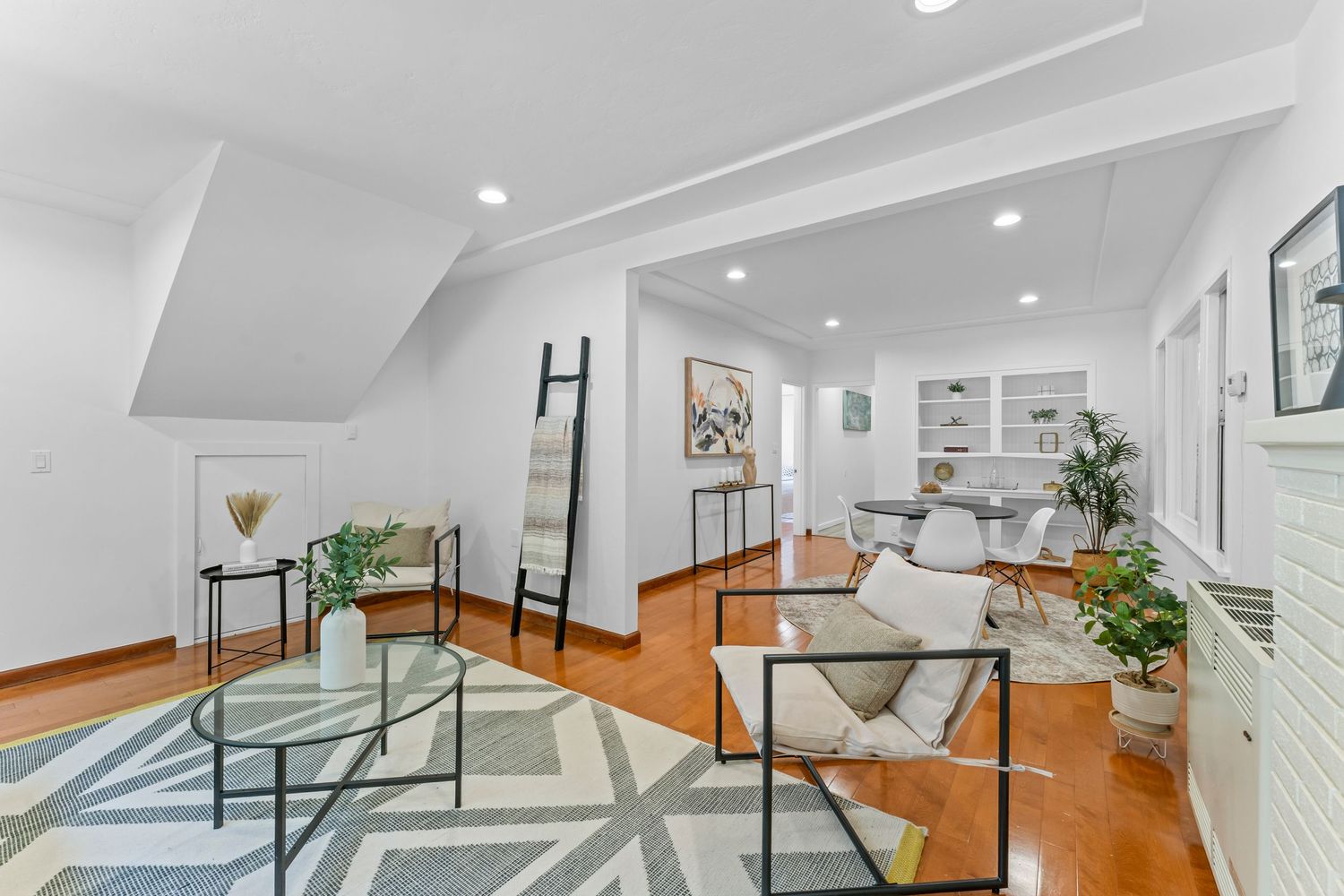 Open living space with geometric area rug, hardwood floors, recessed lighting, glass coffee table, and built-in shelving.