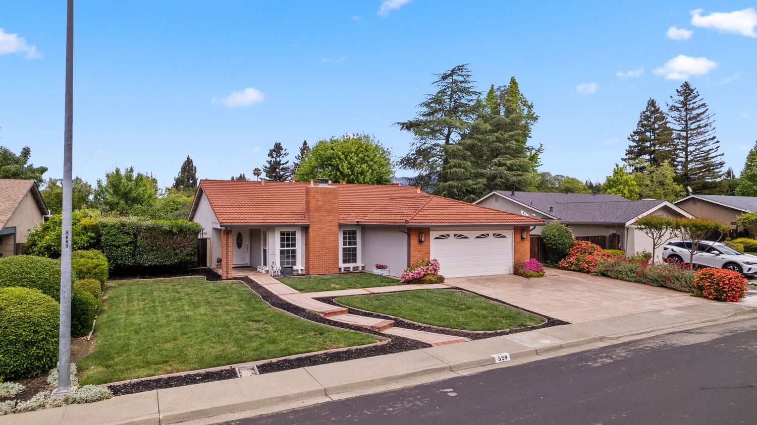 Single-story ranch home with red tile roof, two-car garage, and manicured lawn in a suburban neighborhood.