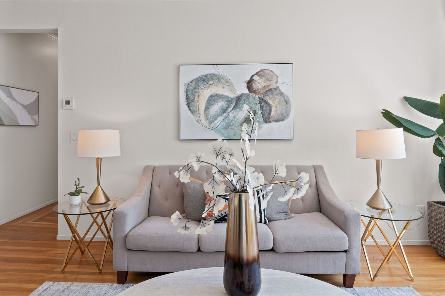 Cozy living room with gray sofa, gold side tables, matching lamps, and ocean-themed wall art on neutral walls.