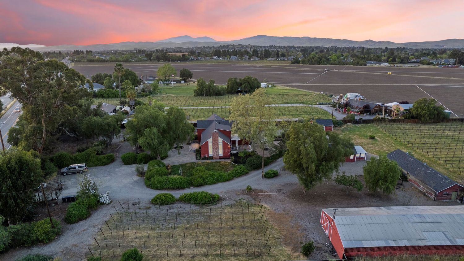 Aerial sunset view of a rural farm property with fields, outbuildings, and mountain backdrop.