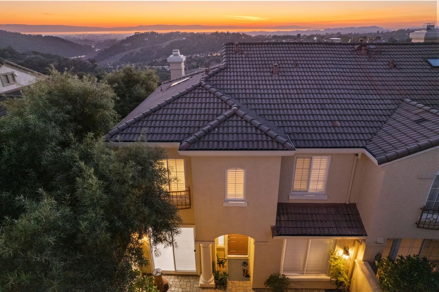 Luxury Mediterranean home exterior at sunset with tile roof, balcony, and hillside views.
