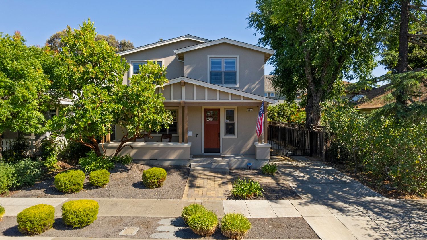 Two-story gray craftsman home with red door, drought-tolerant landscaping, and a paved driveway.