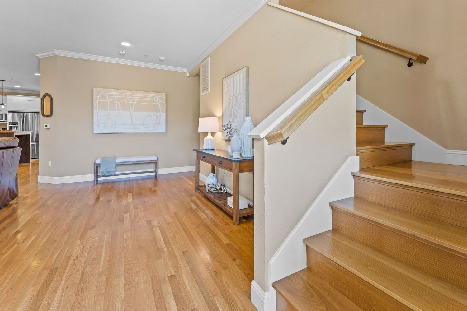 Bright entryway with hardwood floors, white staircase with wood railing, crown molding, and console table.