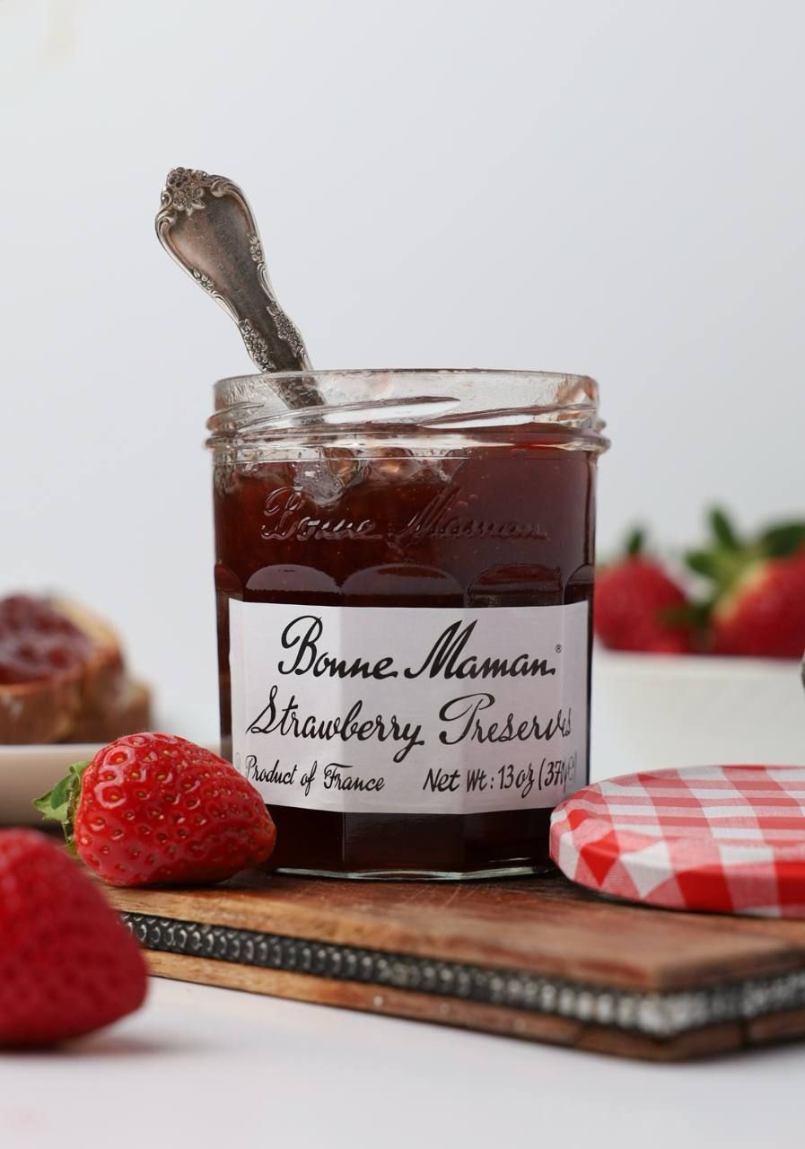 Bonne Maman Strawberry Preserves jar with silver spoon on wooden cutting board with fresh strawberries.