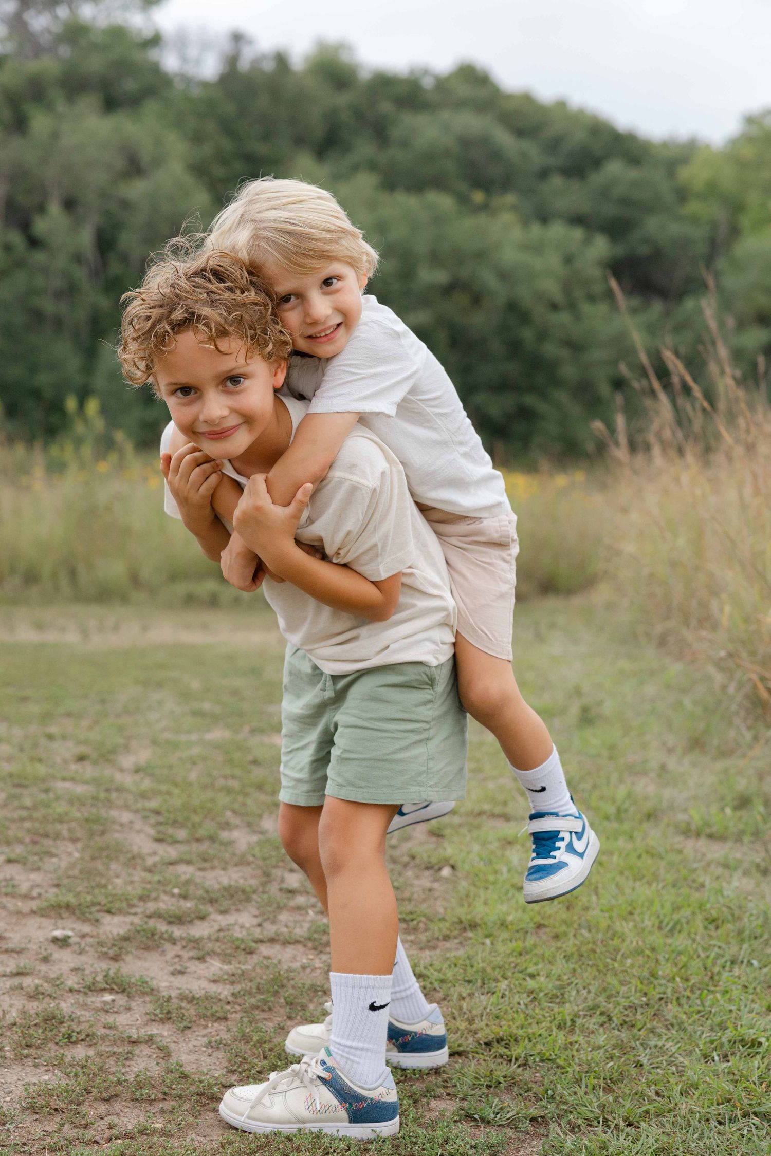 Two young boys playing outdoors, one giving the other a piggyback ride in a grassy field.