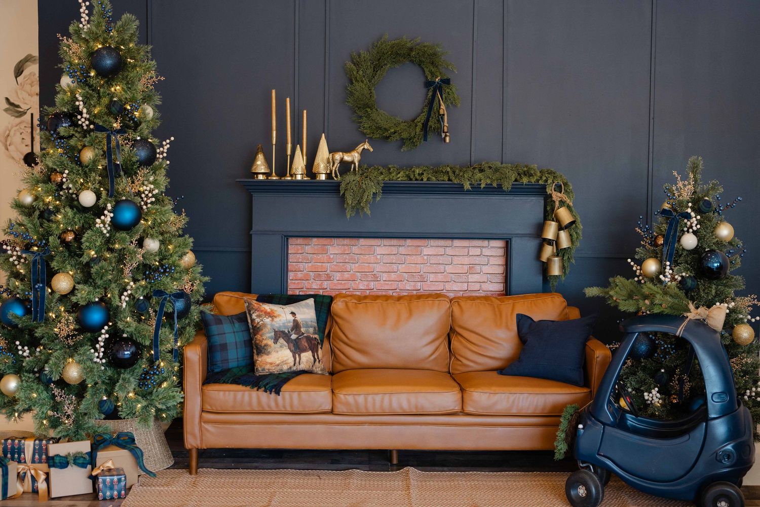Cozy living room with leather sofa, blue cushions, decorated Christmas trees, wreath, and festive mantel decor.