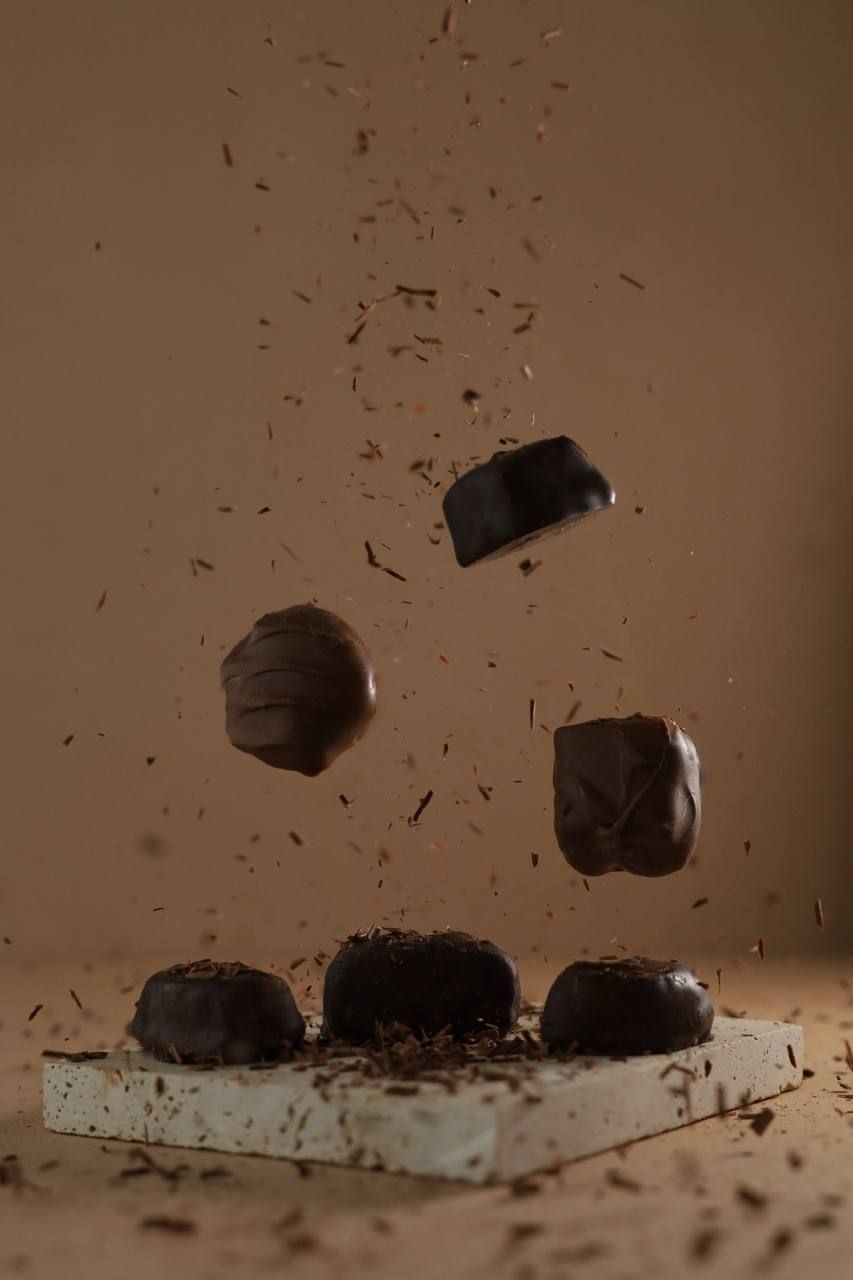 Dark chocolate truffles and candies dramatically floating in mid-air with chocolate shavings on a beige background.