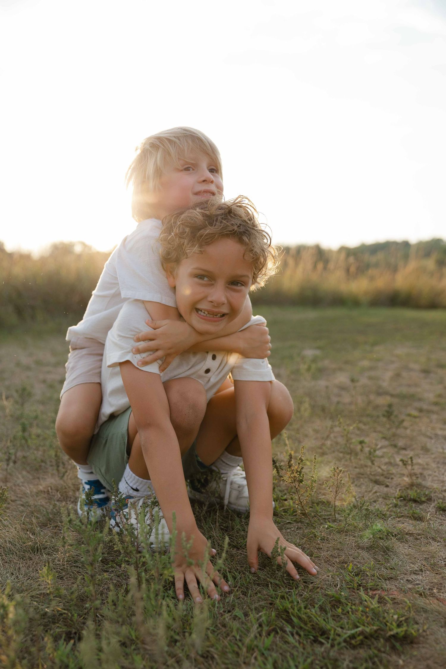 Two happy children playing outdoors in a sunny field, with one boy giving the other a piggyback ride at sunset.