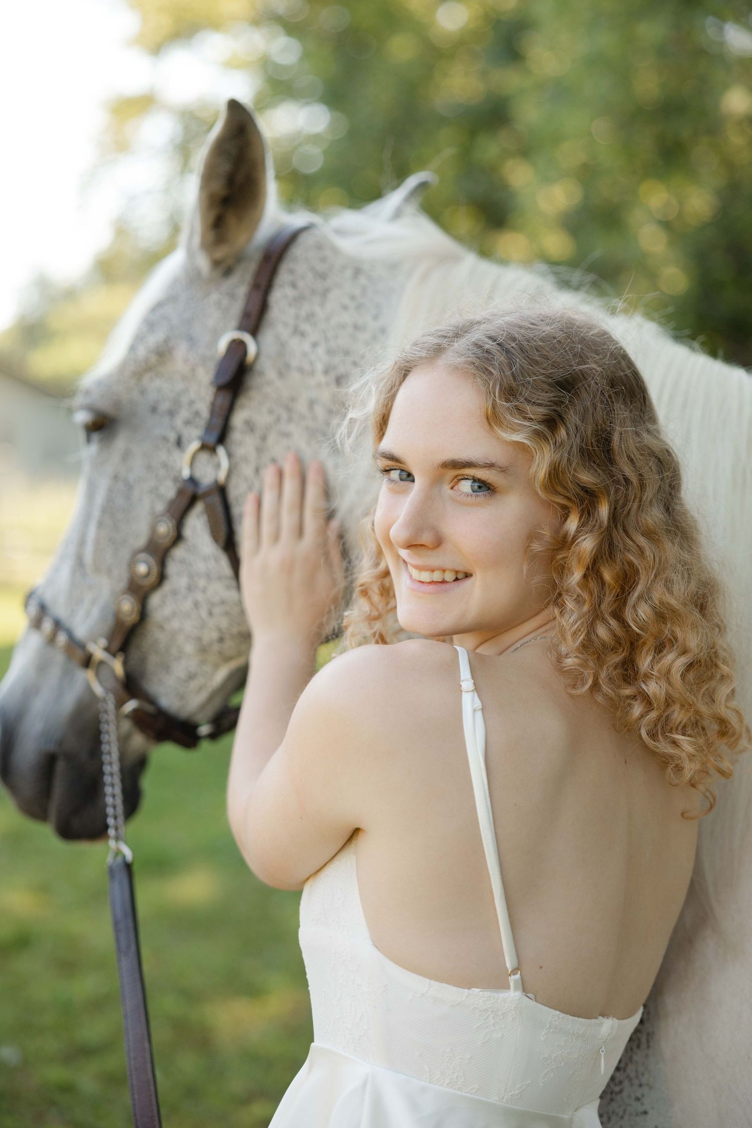 smiling female high school senior in a long white dress with a horse elegant portrait