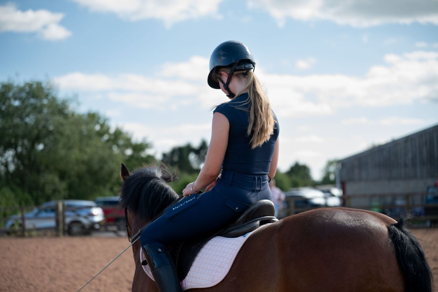 A young female rider in a blue outfit and helmet sits on a bay horse in an outdoor riding arena.