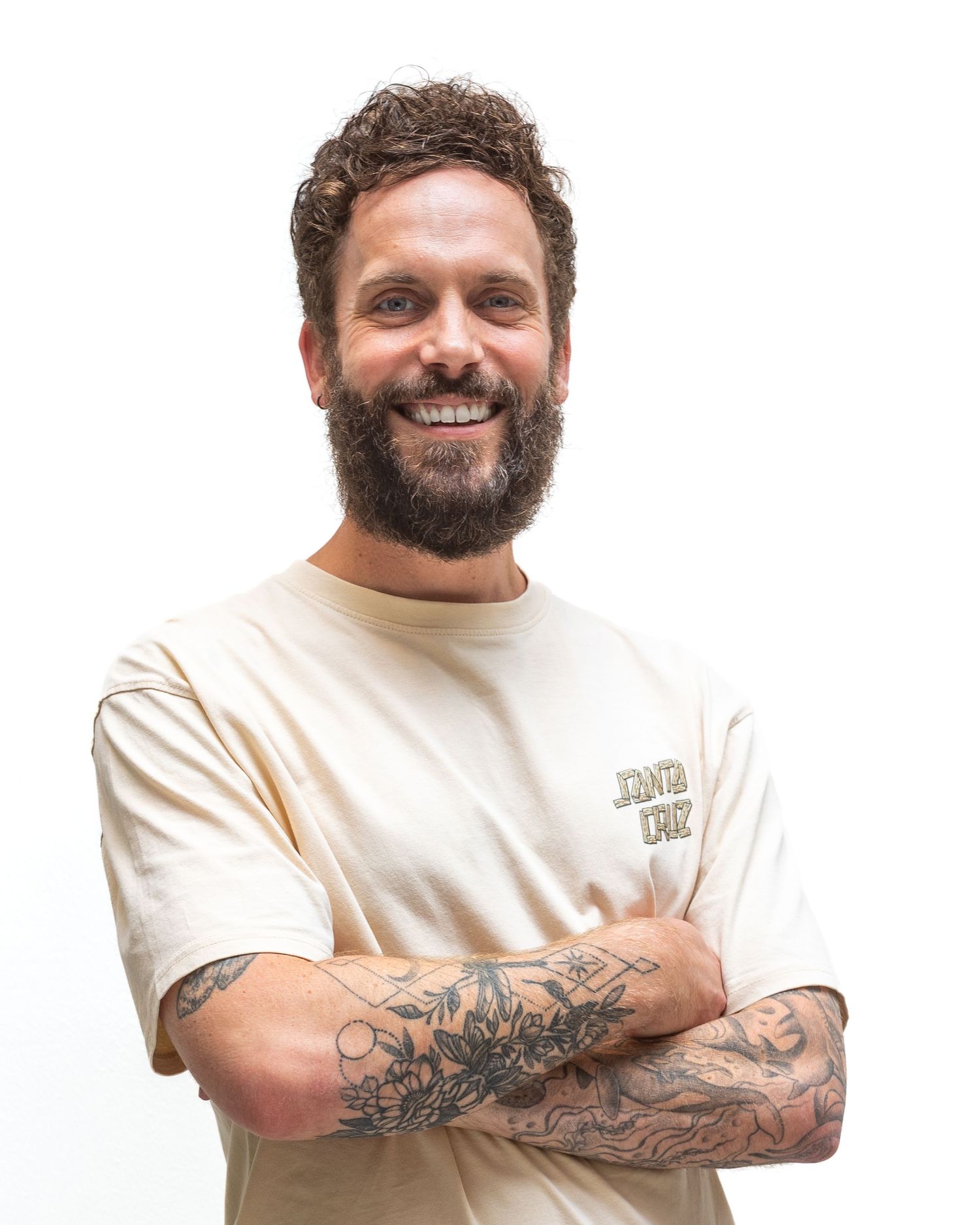 A bearded individual in a white t-shirt smiles in multiple profile views showcasing their tattooed arms.