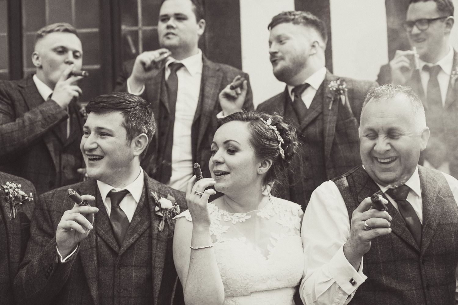 Black and white wedding celebration photo showing a group of well-dressed guests sharing drinks and laughing together.