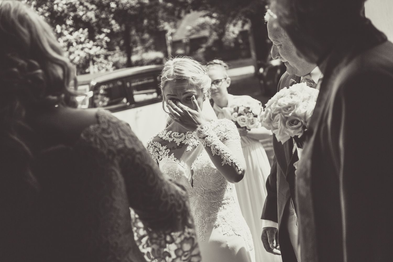 Black and white photo showing a touching candid emotional moment during an outdoor wedding gathering.