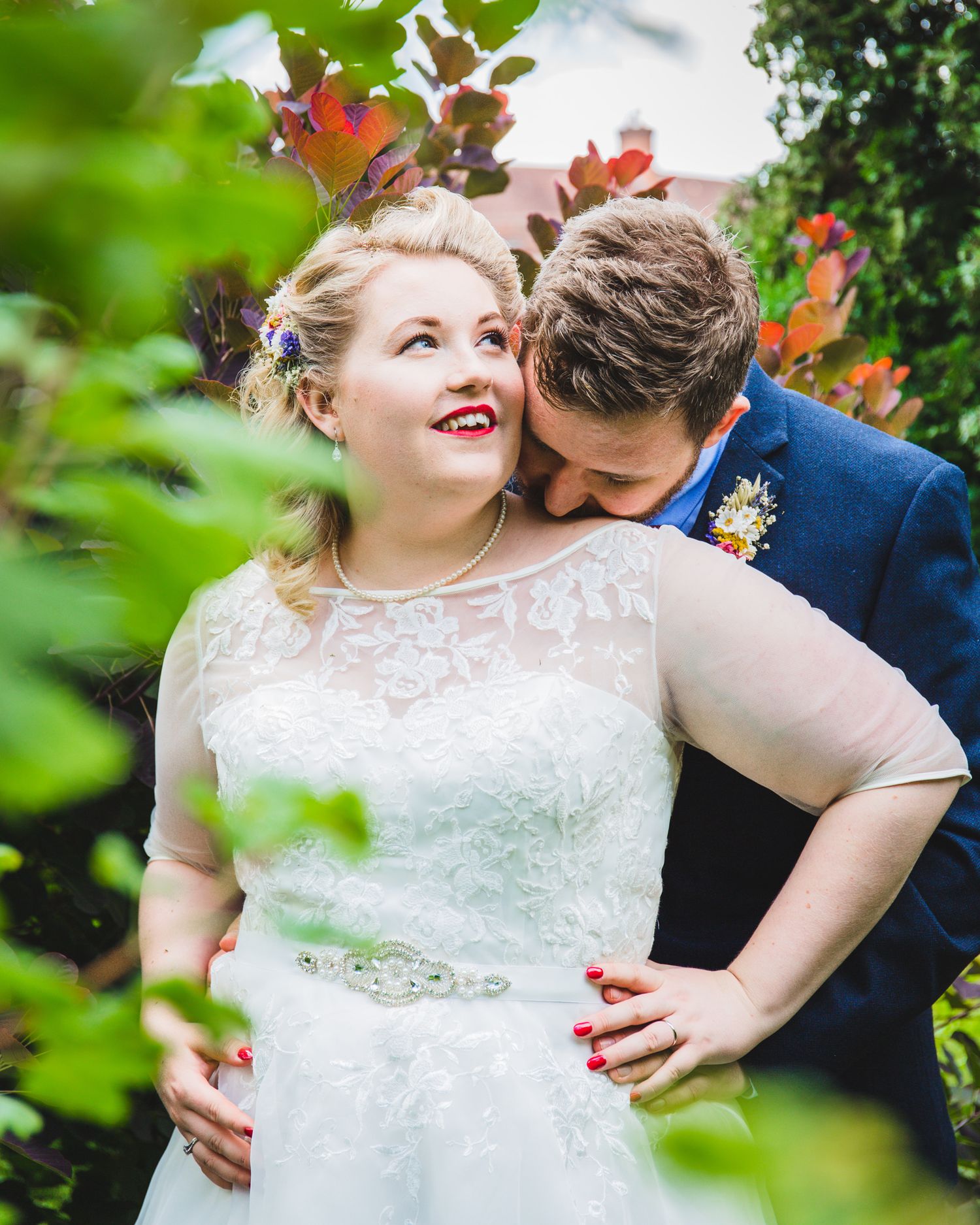 A joyful couple shares an intimate autumn garden moment among colorful fall foliage, the bride wearing a lace wedding gown.