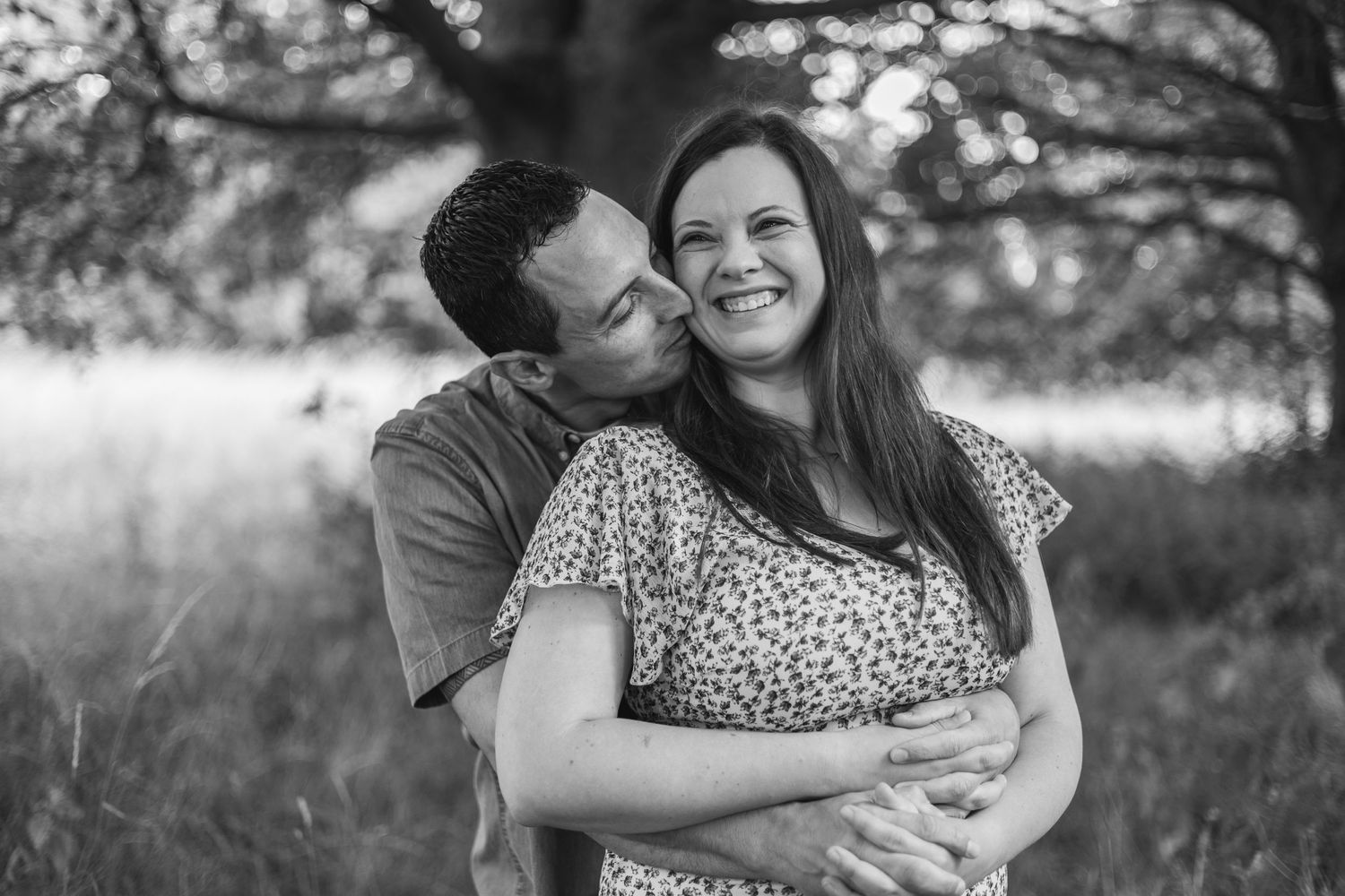 A couple shares a tender embrace in a black and white portrait outdoors.