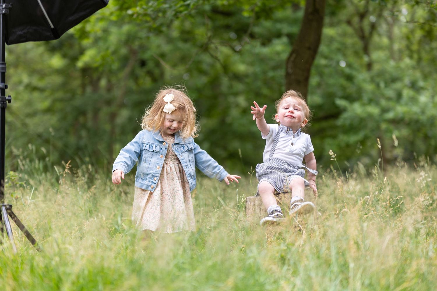 Two children playing and laughing together in a meadow filled with tall grass on a sunny summer day.