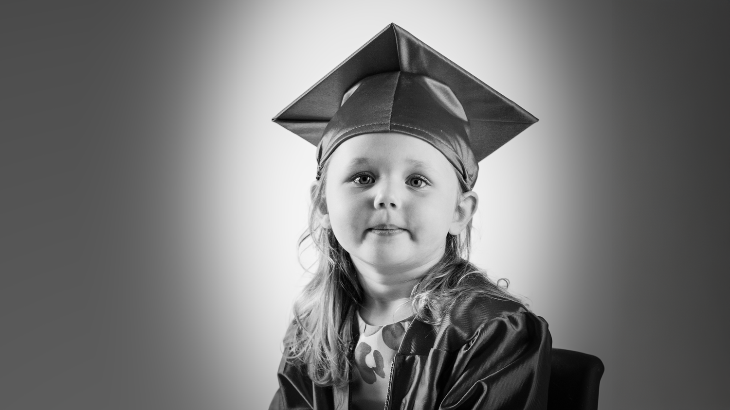 Black and white portrait of a young graduate wearing a cap and gown, looking upward with optimism.