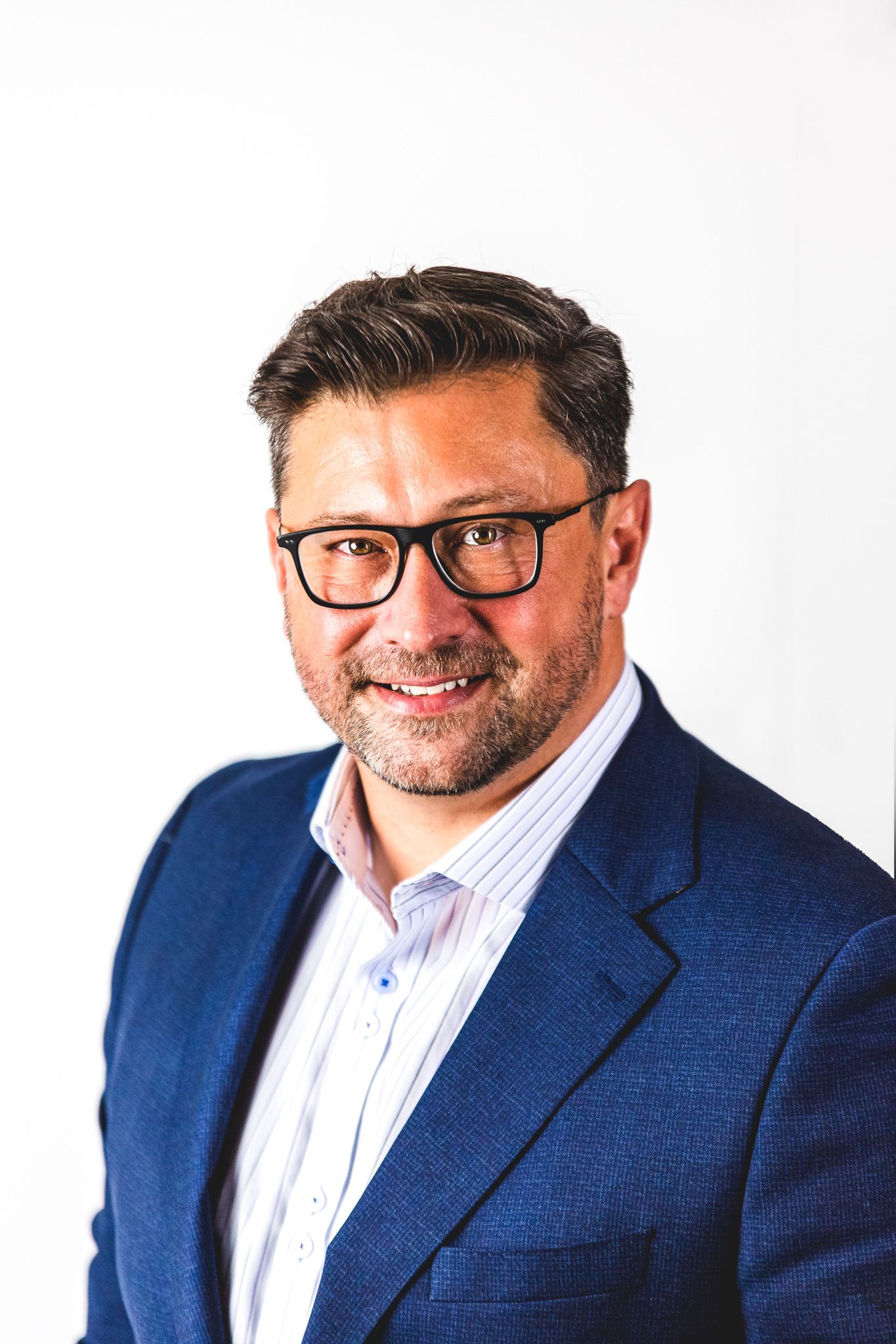 Professional headshot of person in navy blazer and glasses against white background smiling warmly.