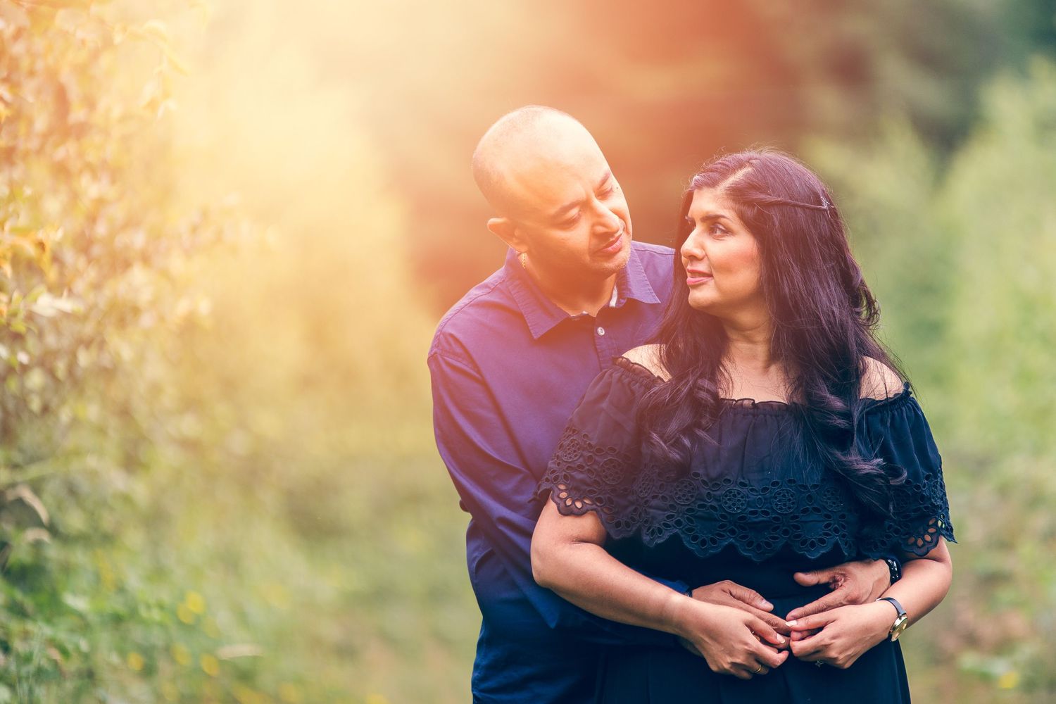 A couple embraces in a romantic sunset moment with warm golden lighting and natural backdrop.