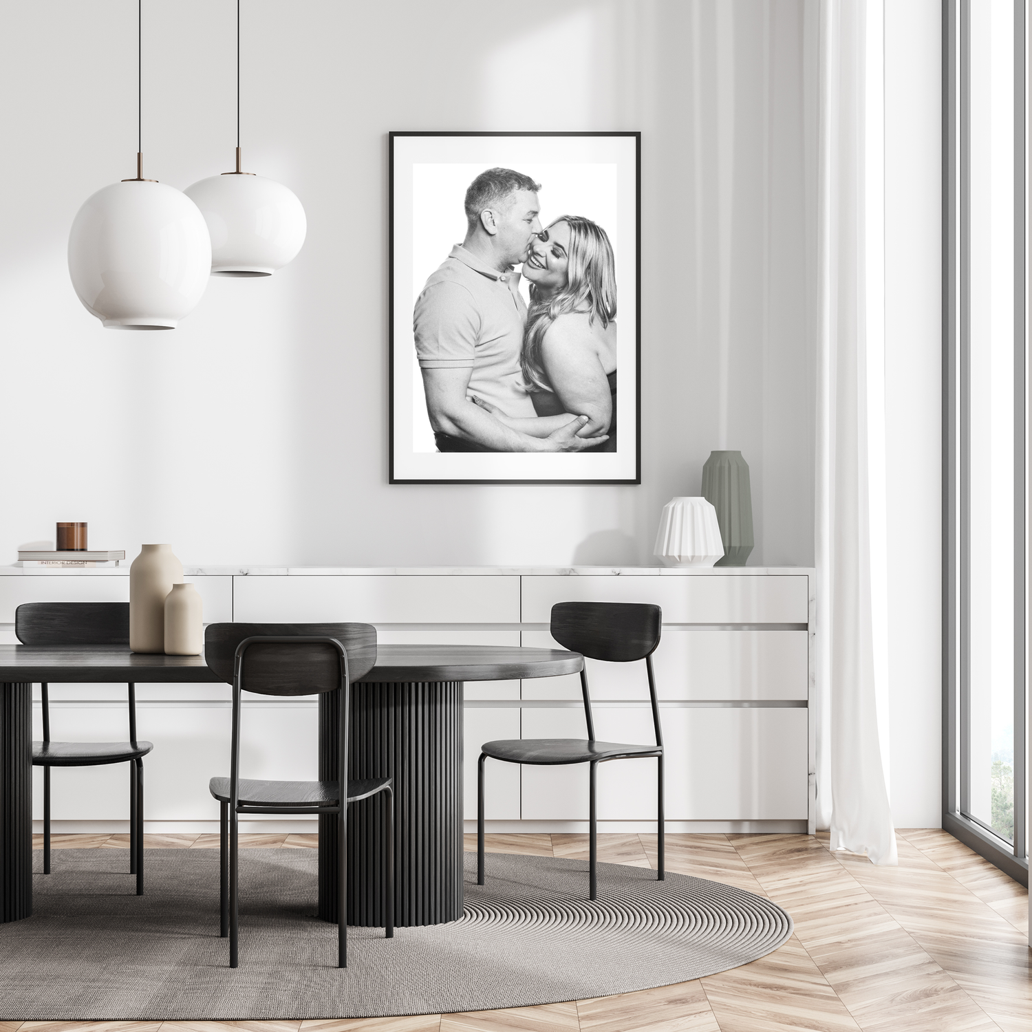 Modern minimalist dining area with black chairs, round table, white pendant lights and black and white portrait on white wall.