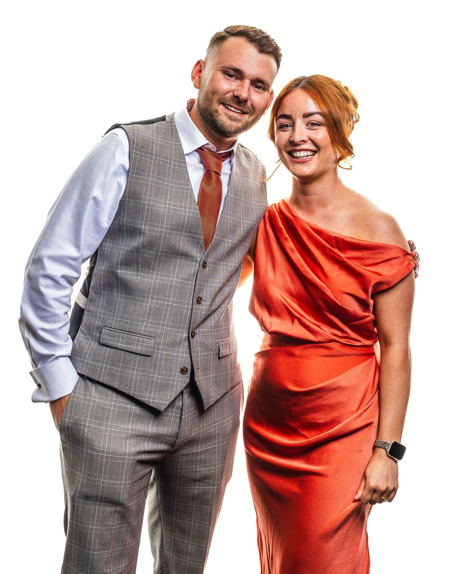 A smiling couple dressed in elegant attire, man in grey vest suit and woman in red satin dress, posing together.