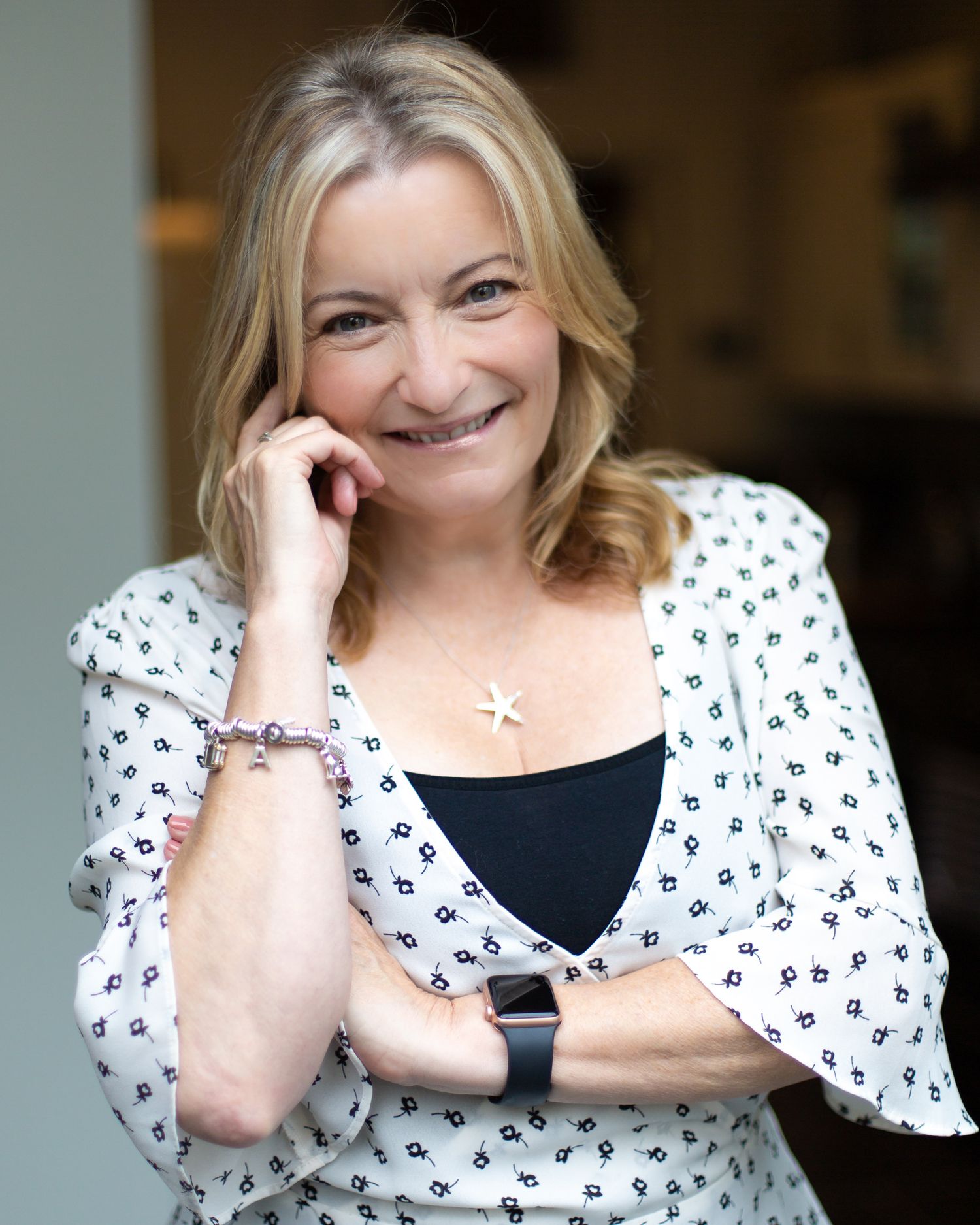 A person wearing a black and white polka dot top and smiling while resting their hand near their face.