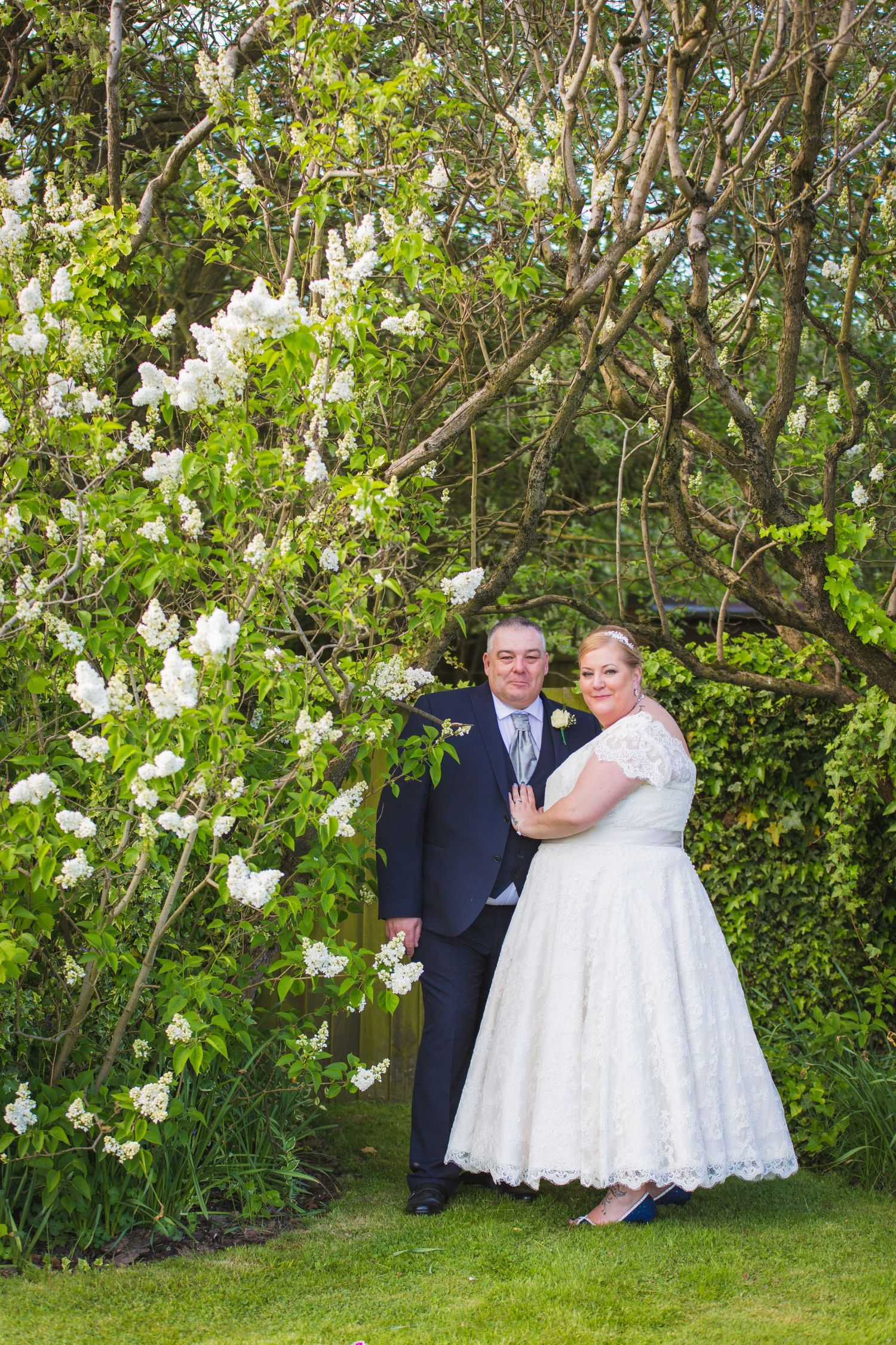 Wedding couple poses by blooming white flowers in garden setting.