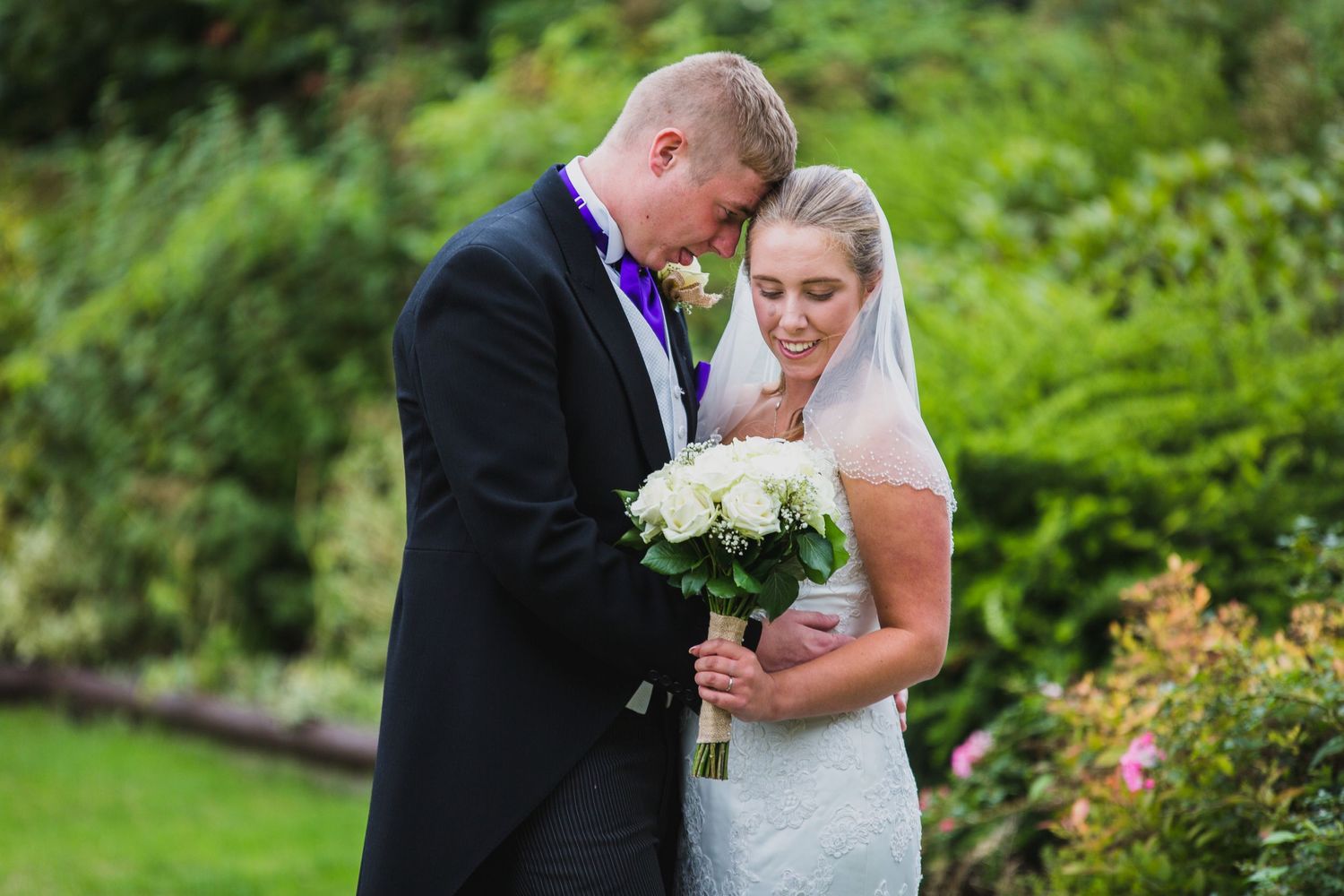 Wedding couple sharing intimate moment outdoors with white bouquet.