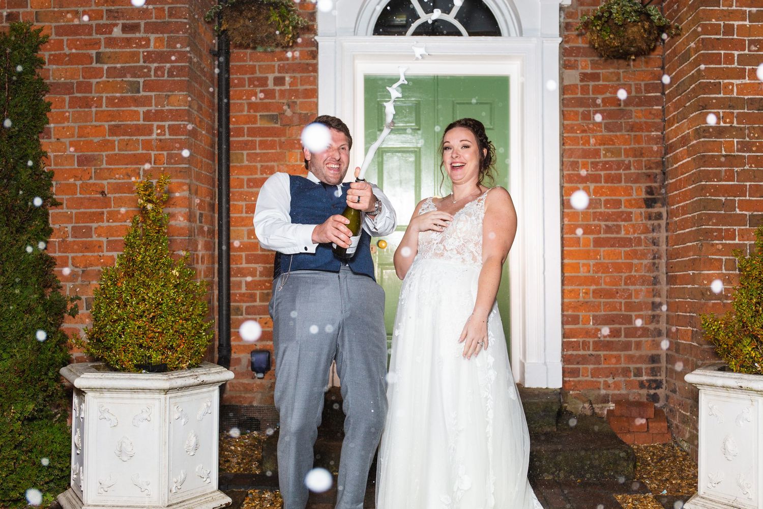 A couple shares a tender moment in front of a white Georgian doorway with red brick walls and winter decor.
