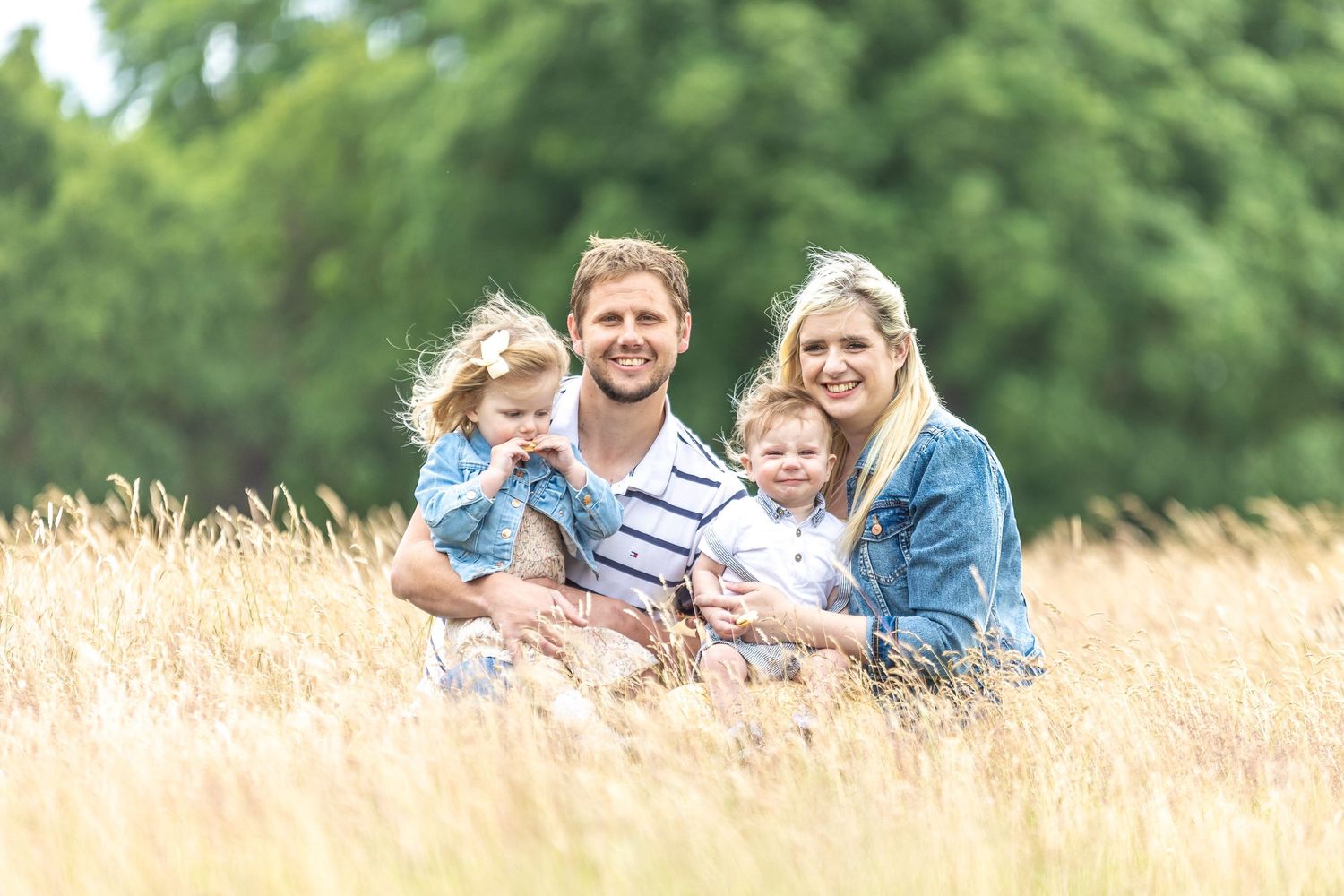 Family smiling together while sitting in a tall grassy field during sunset outdoor photo session.