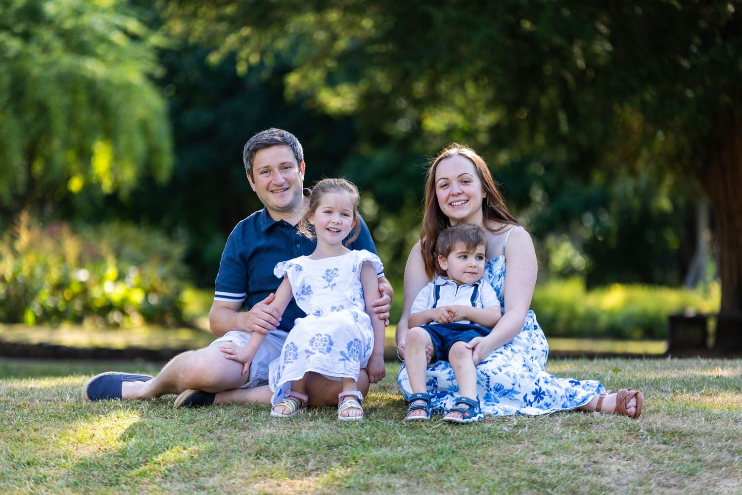 A family sits together on grass in a garden setting during golden hour lighting.