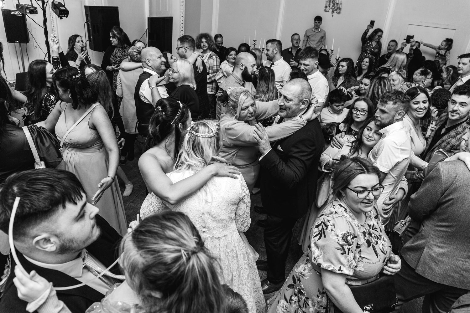 Black and white photo of a crowded dance floor at a wedding reception with guests dancing and celebrating together.
