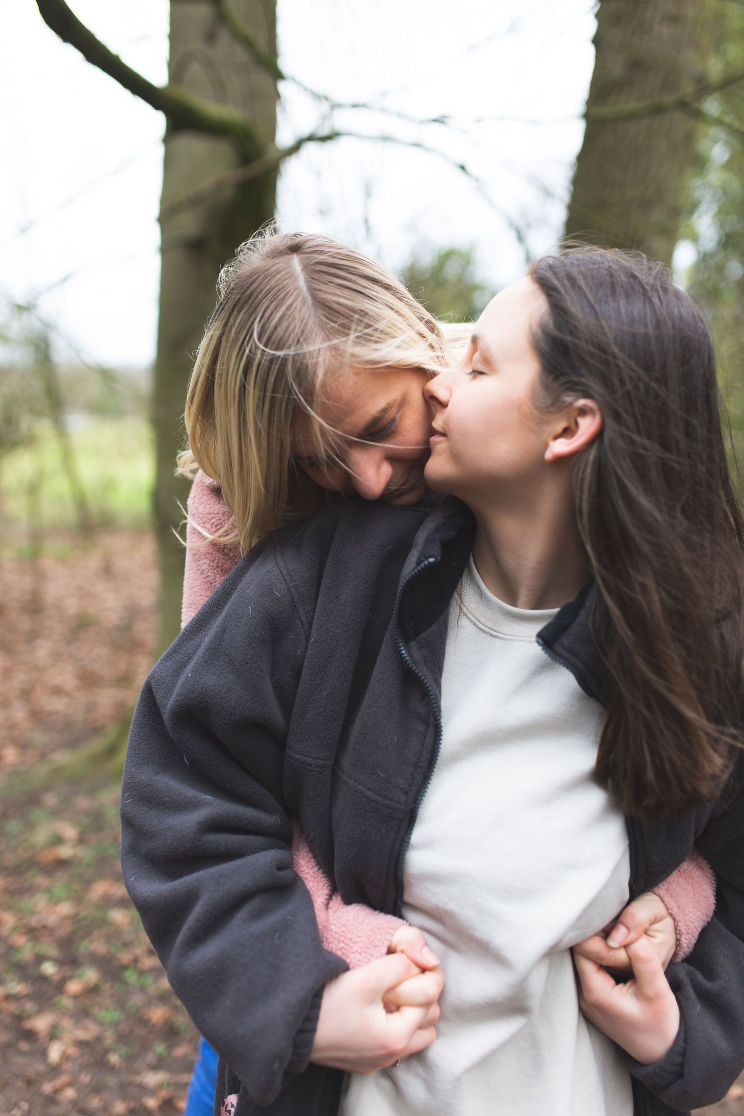 Two people share an intimate moment in a wooded area, with one wearing a dark jacket and the other in white.