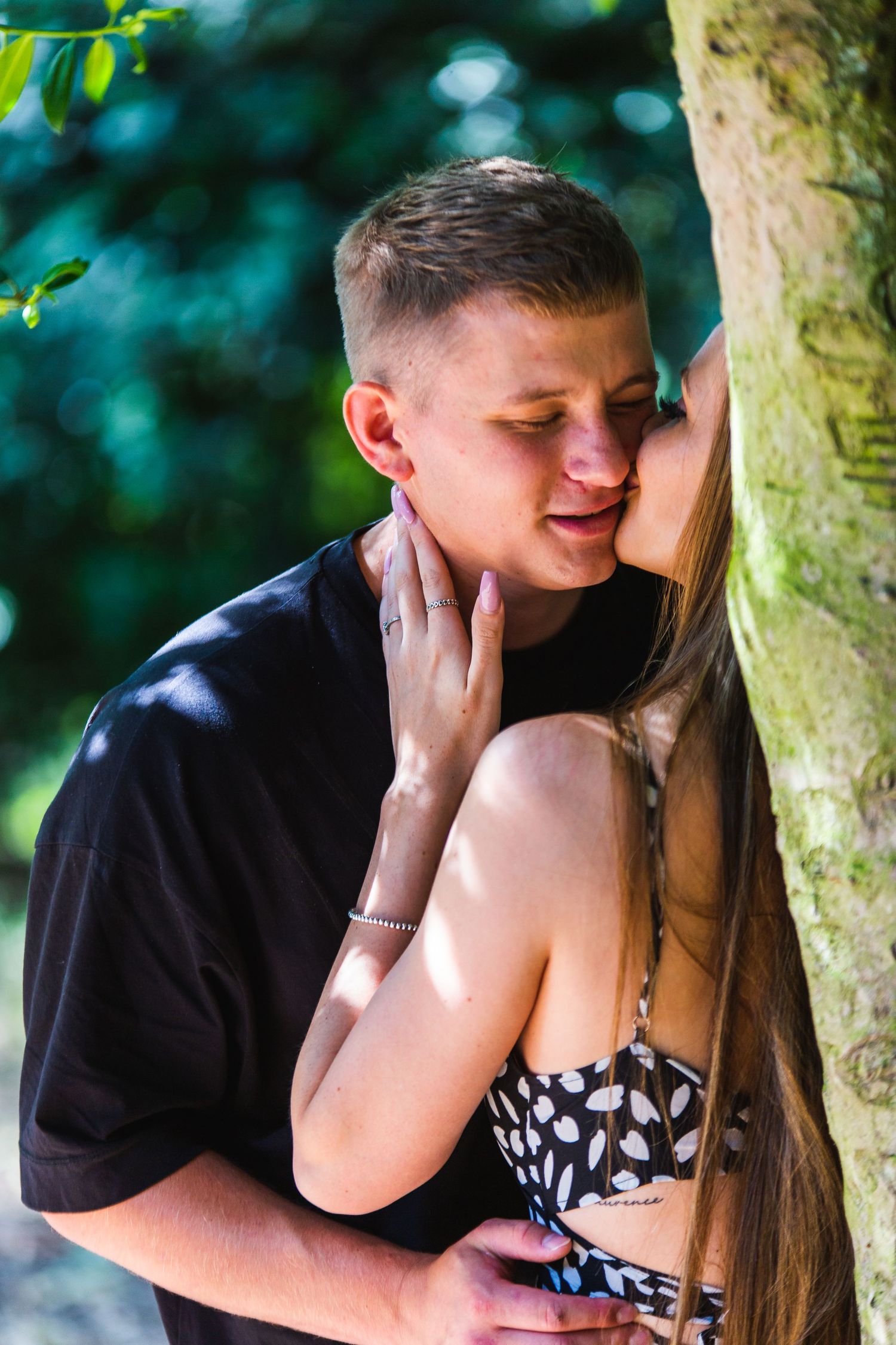 A romantic moment between two people against a tree in natural sunlight.