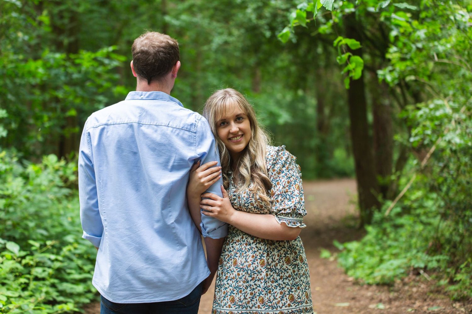 A couple shares a joyful moment together on a walking trail surrounded by green foliage.