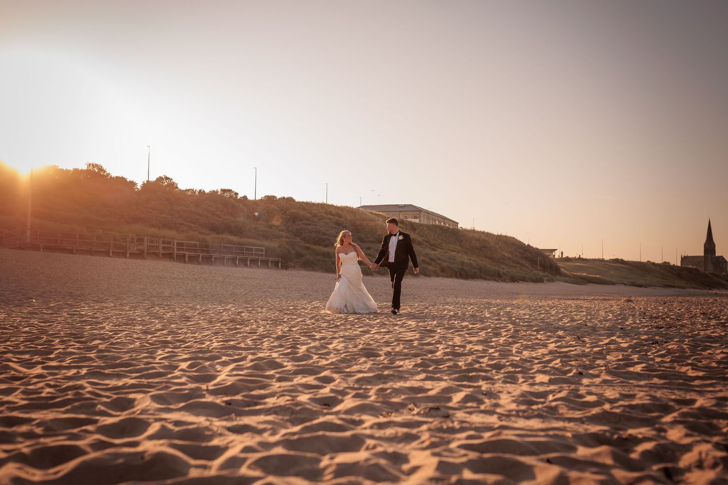 Couple walking on a sandy beach at sunset with warm golden light illuminating their silhouettes against the horizon.