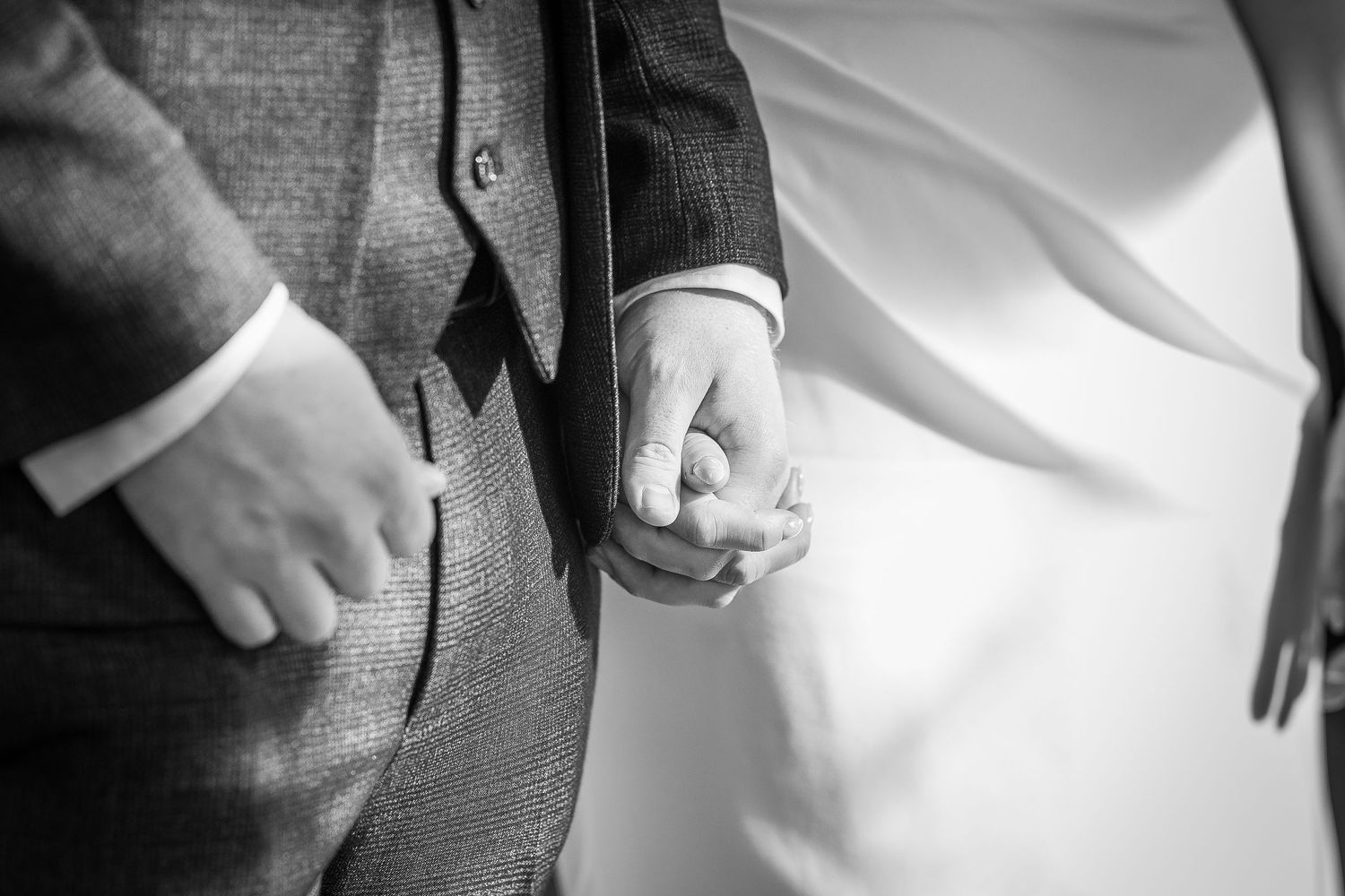 Close-up details of formal attire showing suit jacket, white shirt cuffs, and hands adjusting clothing.