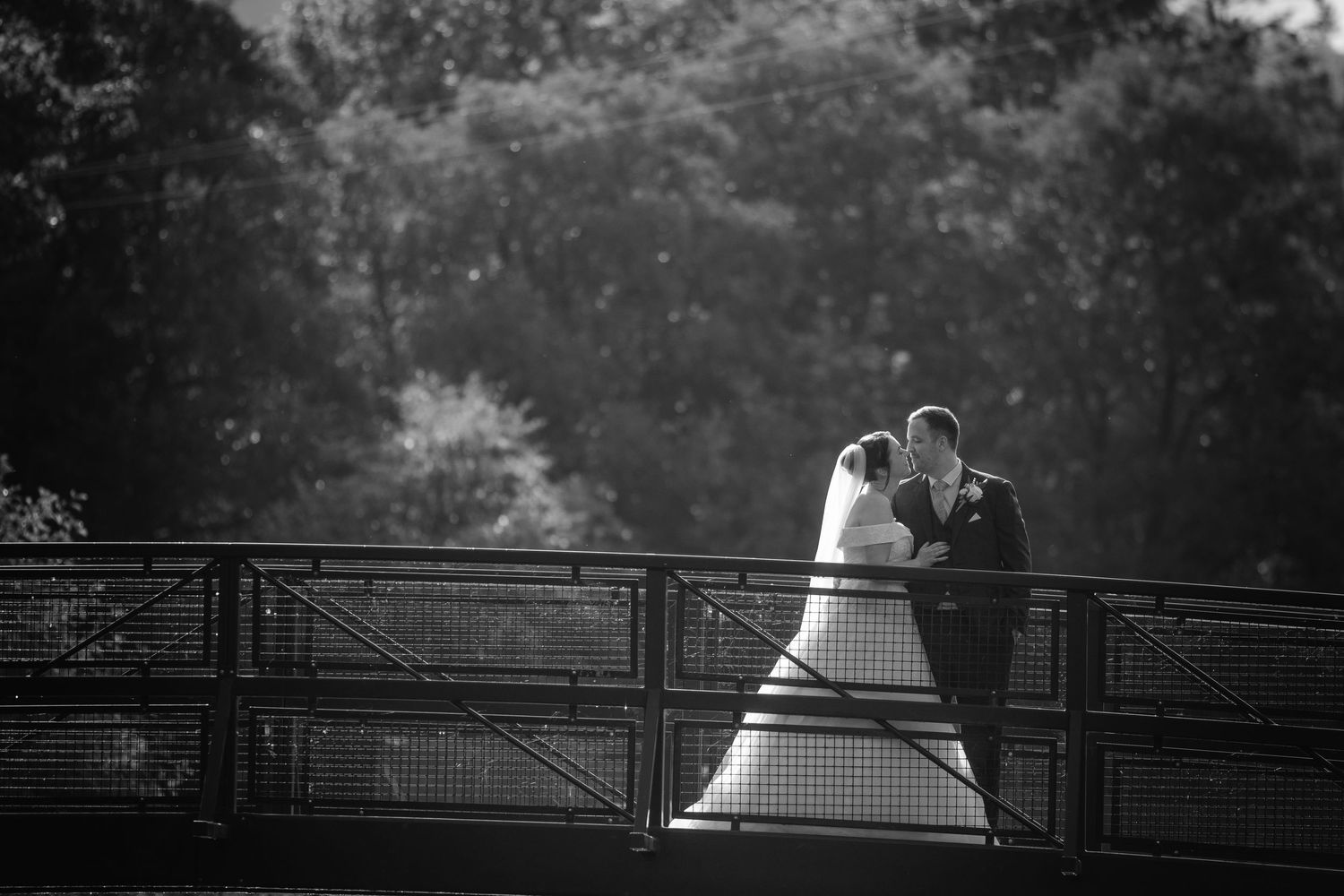 Silhouetted figures kiss against romantic railing backdrop in black and white wedding photograph series.