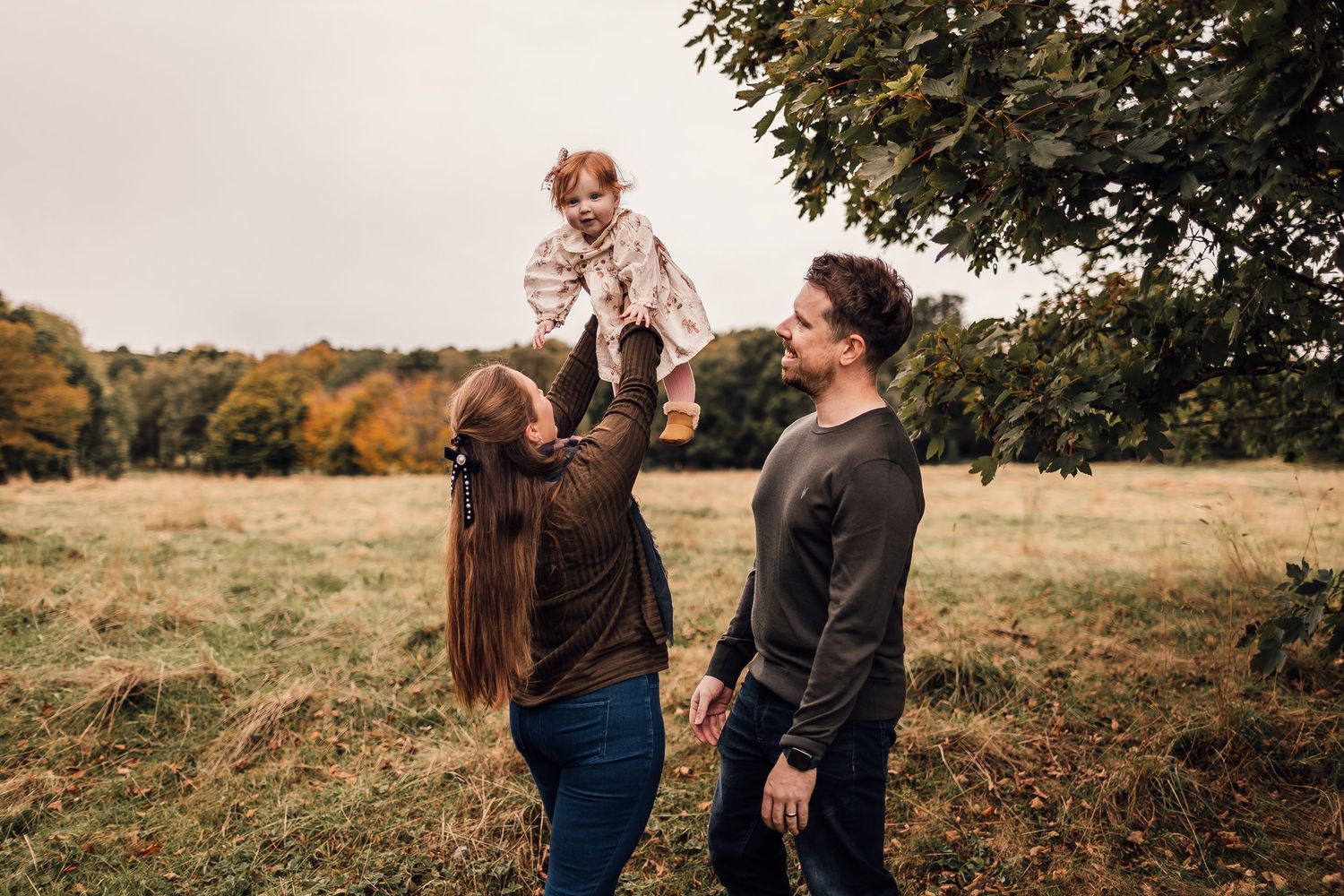 Two people share a romantic moment in an autumn field surrounded by trees during sunset.
