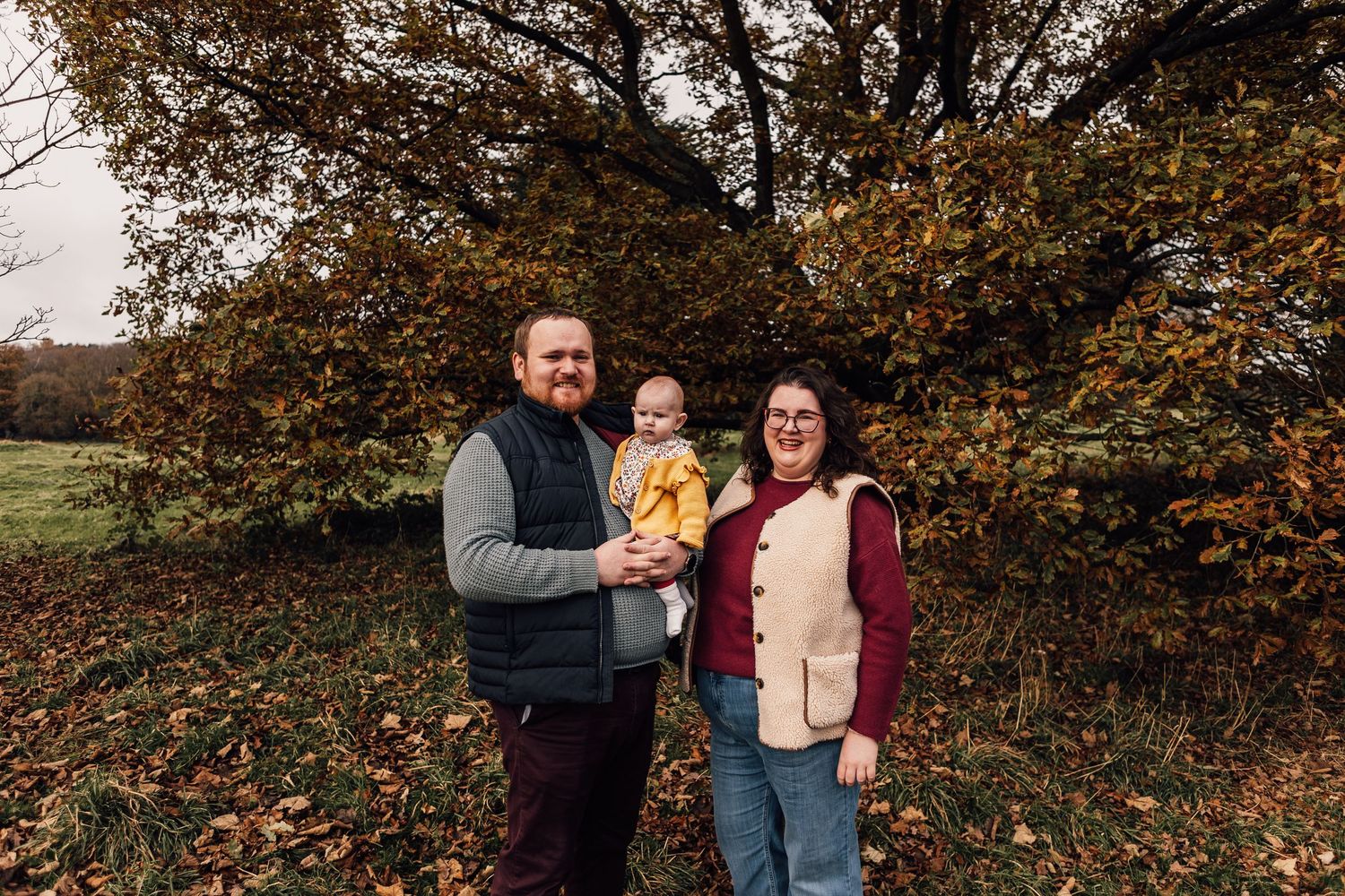 A family enjoying a fall afternoon outdoors together surrounded by autumn trees with colorful foliage.