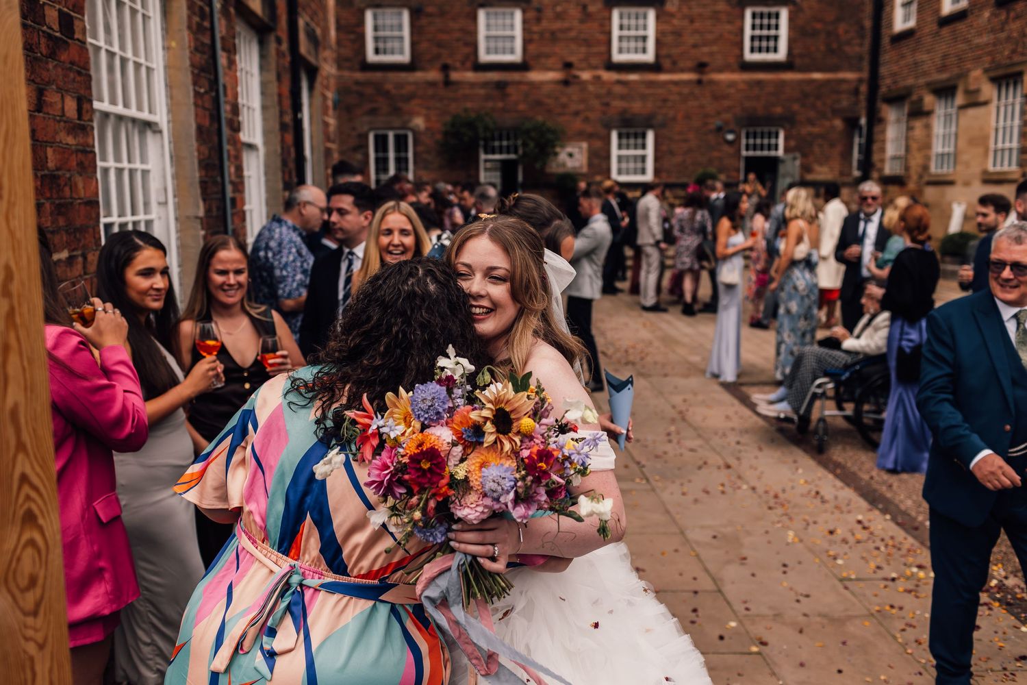 A group of wedding guests gather outside a historic brick building during a celebration.
