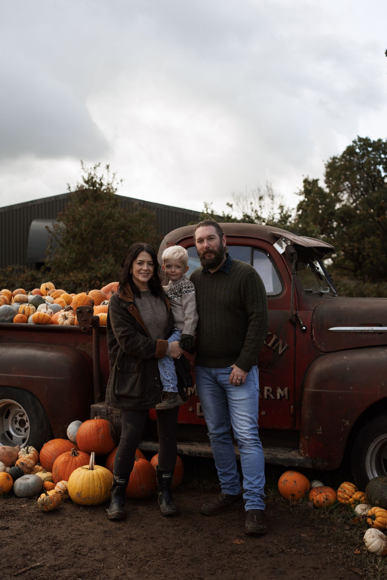 A rustic vintage pickup truck loaded with pumpkins at a fall harvest display under cloudy skies.